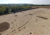 Vue aérienne du site en cours de fouille Au premier plan, un bâtiment sur poteaux sert de couloir d’entrée d’un enclos palissadé. Les Grèves, Beaurieux (Aisne), 2014.