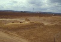 Carrière de granulats alluvionnaires à Soucy (Yonne-89) en cours d'exploitation Surface du gisement alluvionnaire (cailloutis sableux) juste avant son extraction avec :  - en arrière plan, le front de taille de la gravière qui marque  l'épaisseur des  découvertes  (ie. sablon + limon + argile) impropres pour l'exploitation industrielle, enlevée et stockée par l'exploitant en attendant le réaménagement du site ;  - au premier plan, l'emprise en îlot du site du Paléolithique inférieur de Soucy 5 (âge : 300 000 - 350 000 ans) en cours de fouille, compris dans les sables et limons fluviatiles recouvrant le cailloutis à exploiter par les carriers.